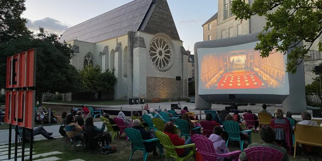 Une cinquantaine de personnes assises dans des fauteuil regardant un écran de cinéma de plein air dans le jardin avec vue sur la Galerie David d'Angers