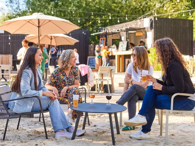 4 femmes assises sur des chaises dans le sable et prenant un verre