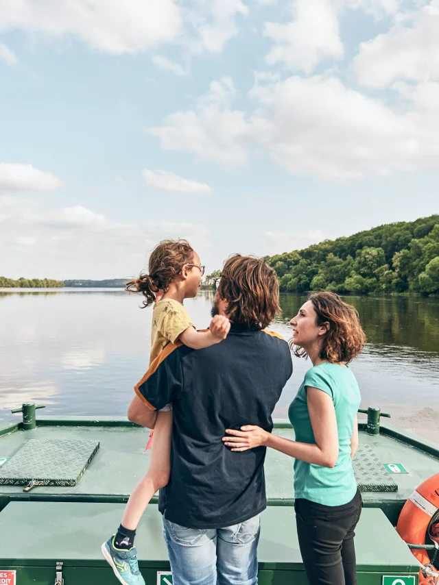 Enfant tenue dans les bras par son père, la mère à côté, à l'avant d'un bateau