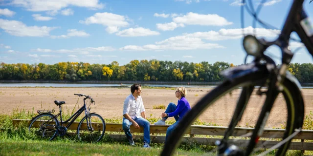 2 people on bikes sitting on a low wall beside the Loire