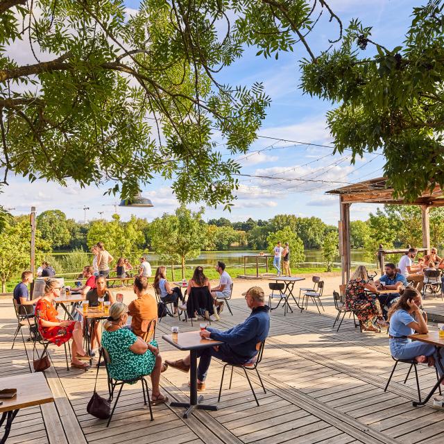 Plan large sur la terrasse et la vue sur la Maine en arrière-plan. Des personnes à tables au premier plan, temps ensoleillé