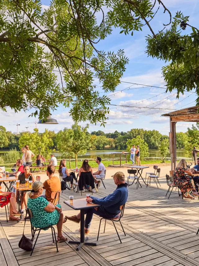 Plan large sur la terrasse et la vue sur la Maine en arrière-plan. Des personnes à tables au premier plan, temps ensoleillé