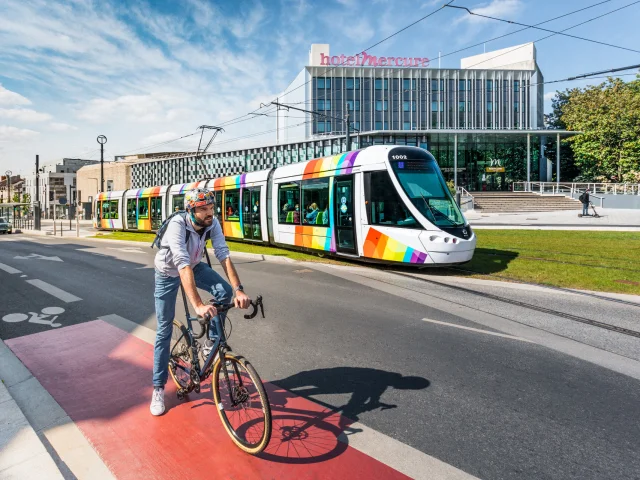 Homme à vélo avec le tram passant derrière, devant le Centre de Congrès d'Angers