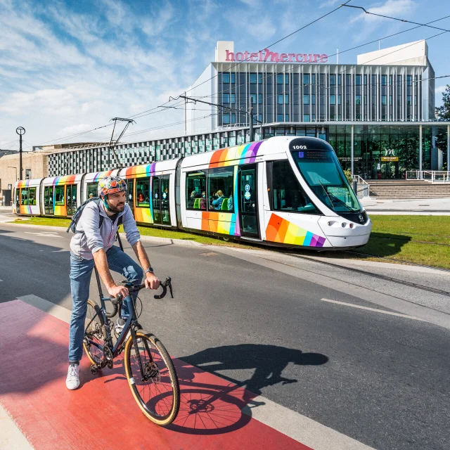 Homme à vélo avec le tram passant derrière, devant le Centre de Congrès d'Angers