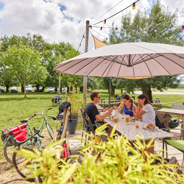 3 personnes à table sur la terrasse d'une guinguette, leurs vélos contre la rembarde