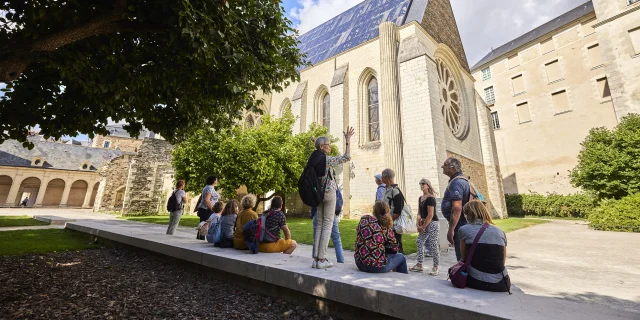 Face à la Galerie David d'Angers, plusieurs personnes assises ou debout face à une guide qui parle, les bras en l'air.