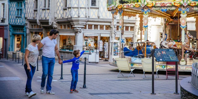 Un couple et un enfant passant sur la place, l'enfant montre le manège