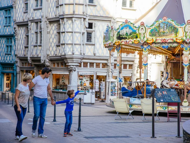 Un couple et un enfant passant sur la place, l'enfant montre le manège