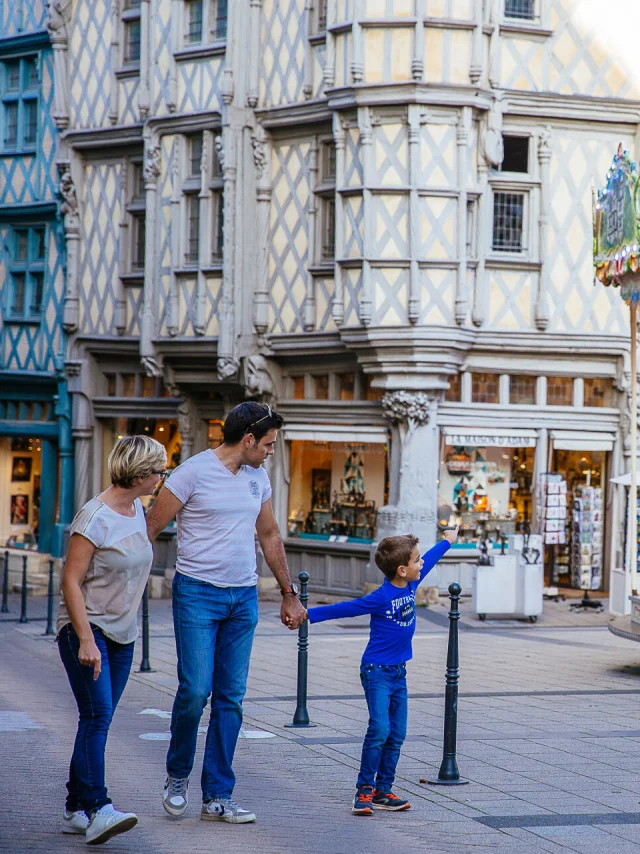 Un couple et un enfant passant sur la place, l'enfant montre le manège