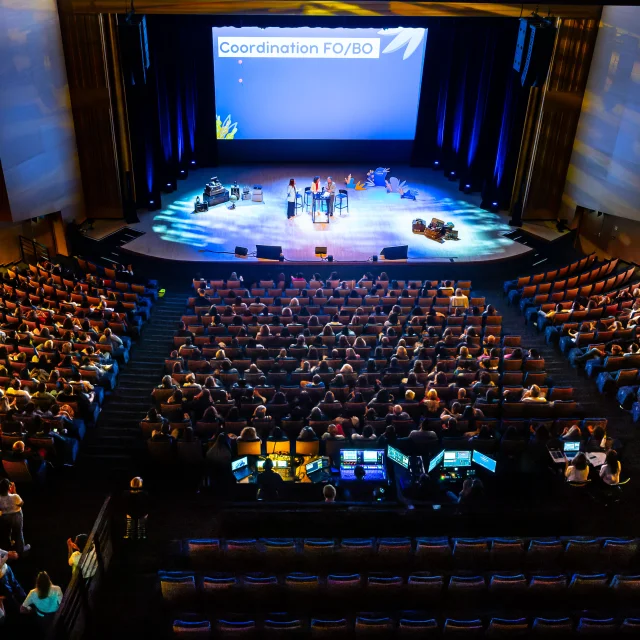 Plan large en plongée du grand auditorium dans le noir, seule la scène est éclairée