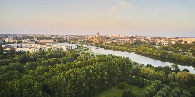 Vue aérienne sur un parc au premier plan, la Maine puis la ville d'Angers à l'arrière-plan, ciel rosé