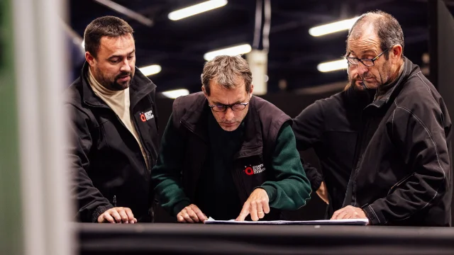 3 hommes vus de face lors qu'ils consulent un plan sur une table