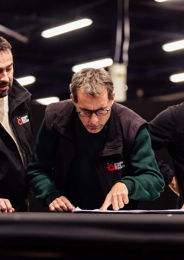 3 hommes vus de face lors qu'ils consulent un plan sur une table