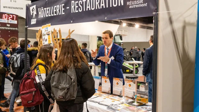 Jeunes discutant avec un homme qui tient un stand sur les formations à la restauration