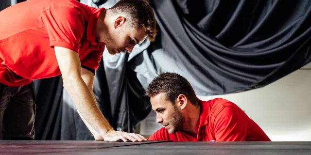 Deux hommes avec un tee-shirt rouge travaillent sur un bloc noir