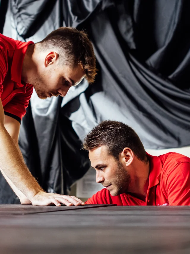 Deux hommes avec un tee-shirt rouge travaillent sur un bloc noir