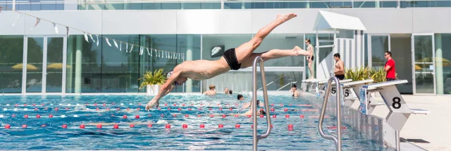 Toma un hombre que se zambulle en la piscina al aire libre en un día soleado