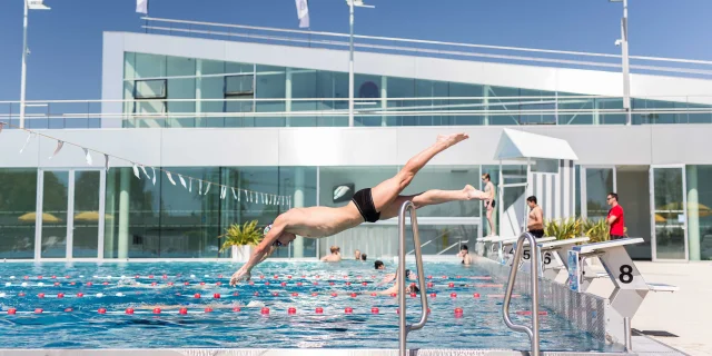 Wide shot of a man diving into the outdoor swimming pool, sunny weather