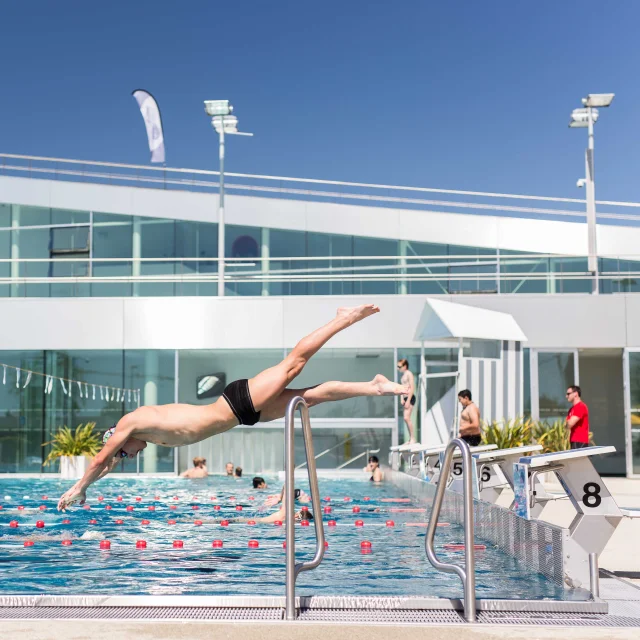 Toma un hombre que se zambulle en la piscina al aire libre en un día soleado