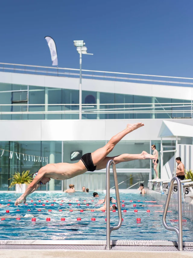 Wide shot of a man diving into the outdoor swimming pool, sunny weather