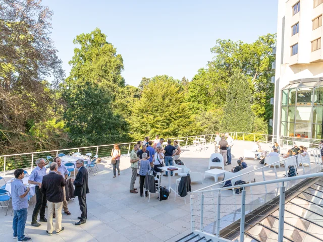 Personnes assistant à un cocktail sur la terrasse ensoleillée avec vue sur le jardin des plantes