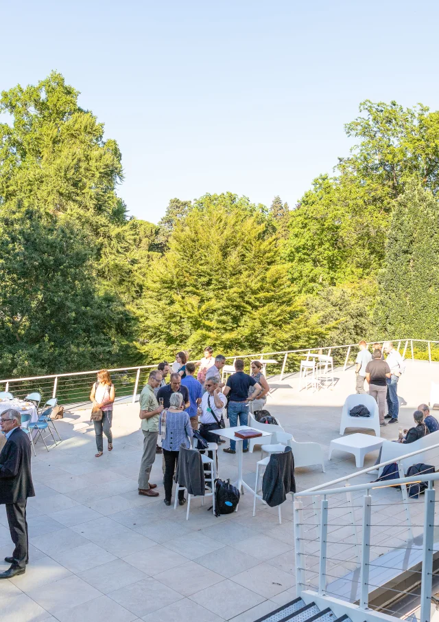 Personnes assistant à un cocktail sur la terrasse ensoleillée avec vue sur le jardin des plantes