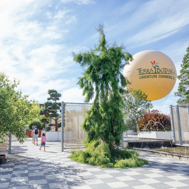 Plan large du parc avec une famille qui se promène et le gros ballon jaune en arrière-plan en l'air