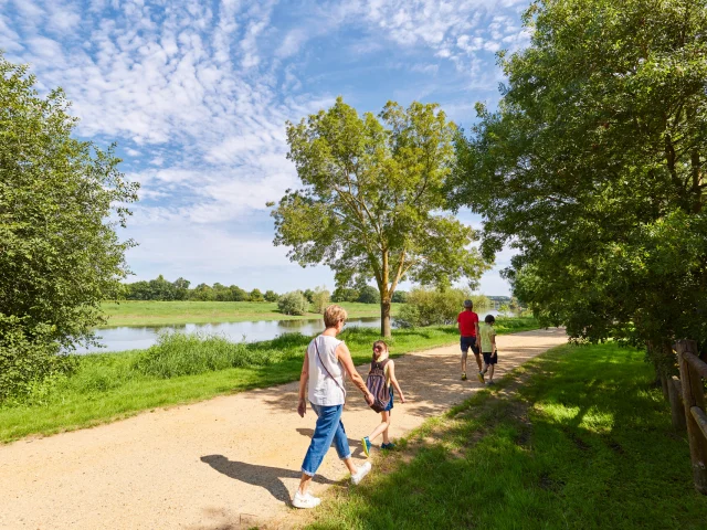 Une famille de 2 adultes et 4 enfants, de dos, marchent sur le chemin qui longe la rivière