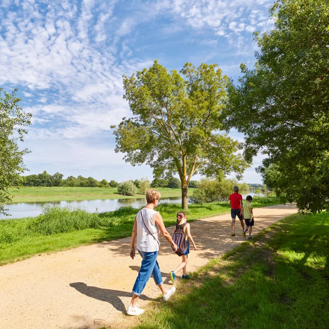 Une famille de 2 adultes et 4 enfants, de dos, marchent sur le chemin qui longe la rivière