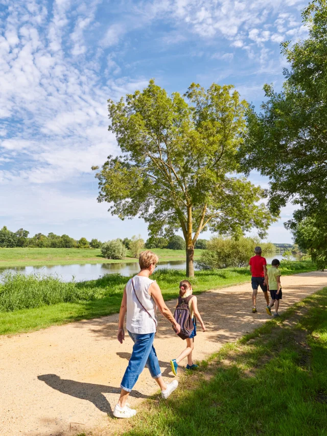 Une famille de 2 adultes et 4 enfants, de dos, marchent sur le chemin qui longe la rivière