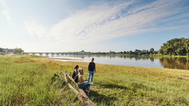 2 personnes assies et une debout sur les bords de la Loire avec un pont au loin