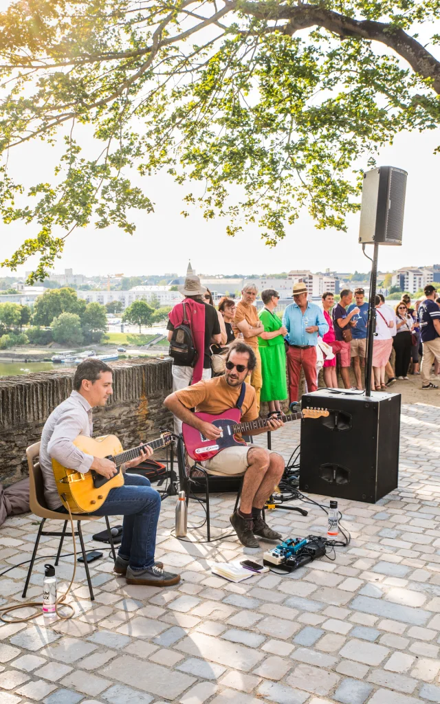 Musiciens jouant assis de la guitare sous un arbre à l'ombre devant quelques spectateurs