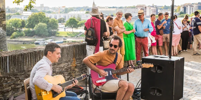 Musiciens jouant assis de la guitare sous un arbre à l'ombre devant quelques spectateurs