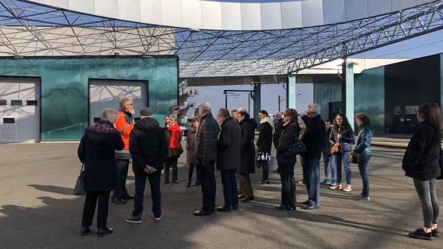 Groupes de personnes rassemblée devant un bâtiment et qui écoutent un homme vêtu de rouge parler