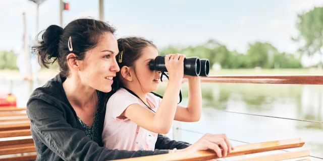 Jeune fille regardant aux jumelles dans les bras de sa mère, durant une croisière sur la Loire