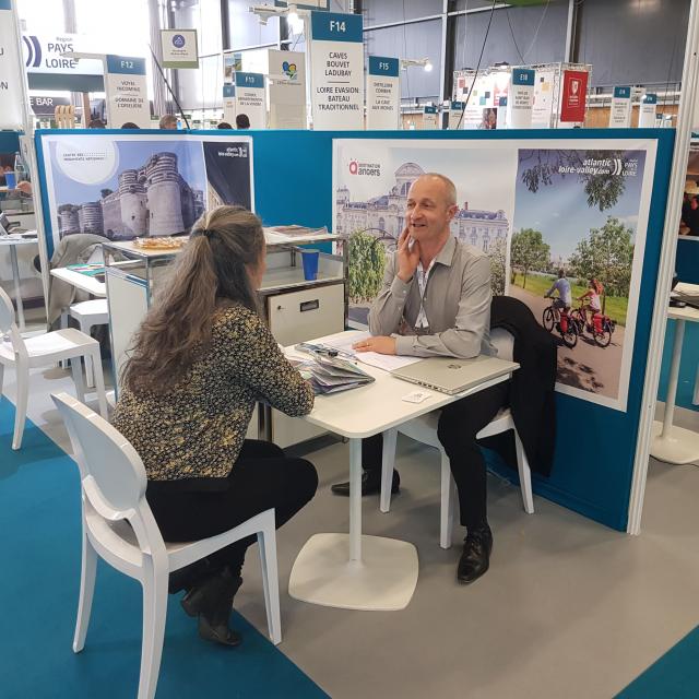 Plan large du stand de Destination Angers au salon Rendez-vous en France, 2 personnes discutant à une table