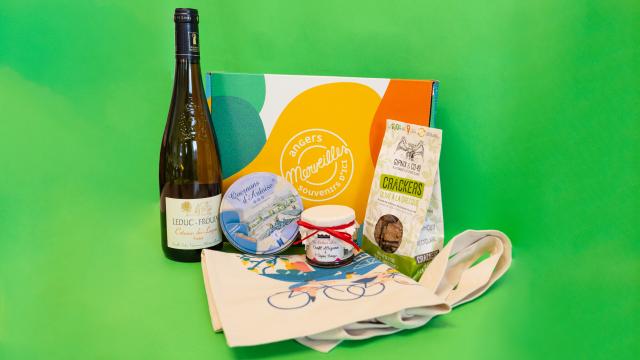 Pack cadeau avec une bouteille de vin, une boîte de Quernon d'ardoise, un pot de confiture, un sachet de crackers et un totebag, posés devant la boîte cadeaux