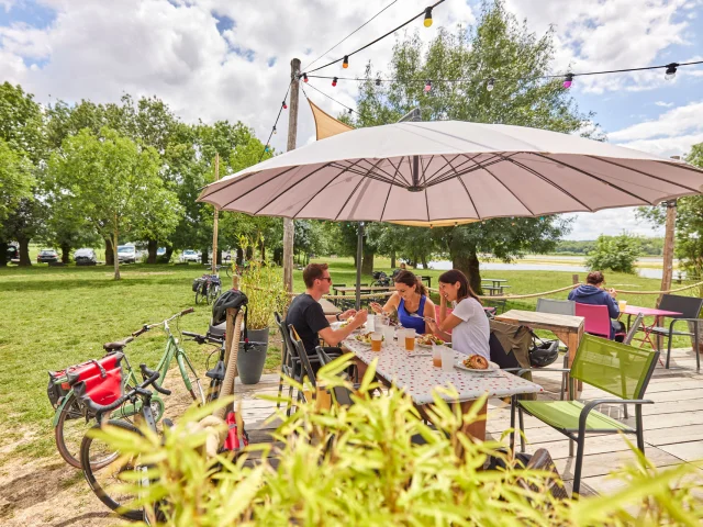 3 personnes à table en terrasse d'une guinguette, leurs vélos posés à côté