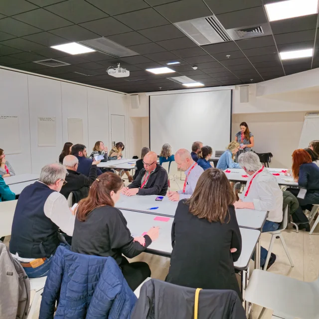 Plan large de la salle composée de tables de travail avec plusieurs personnes assises autour de chacune d'elles